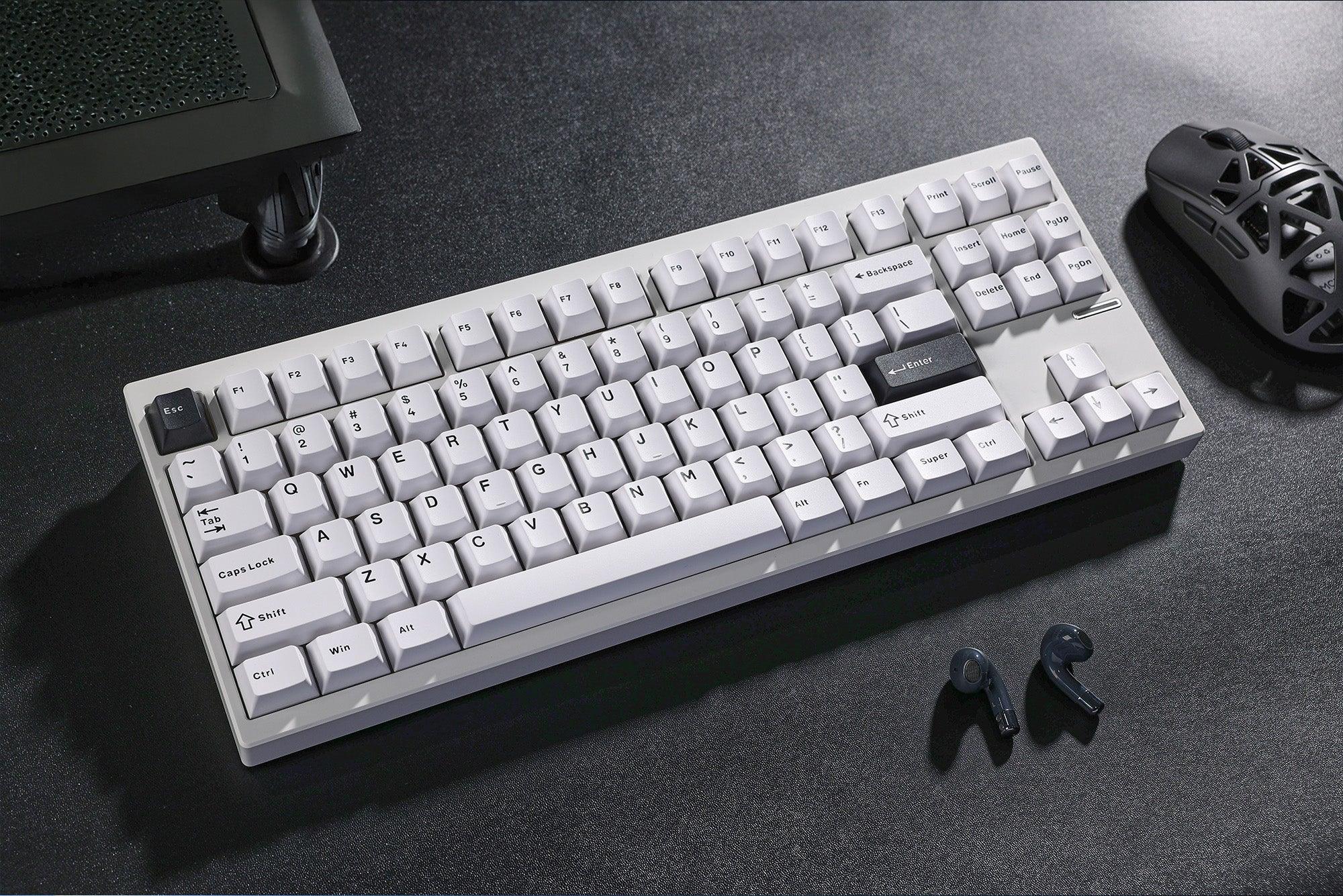 White mechanical keyboard with black accent keys, ergonomic mouse, and wireless earbuds on dark desk