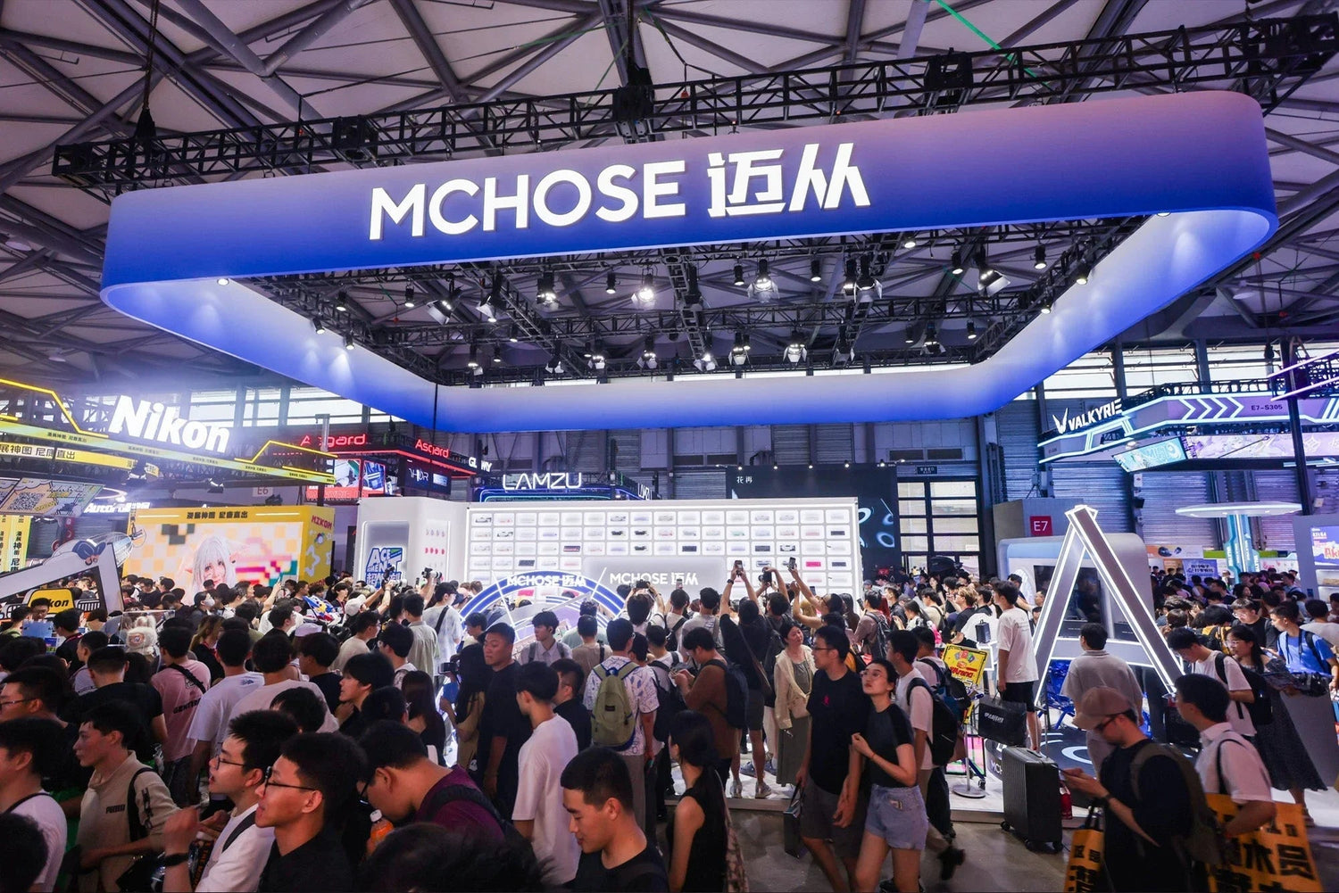 MCHOSE booth at tech expo with crowd, showcasing gaming peripherals and audio devices under modern blue signage.