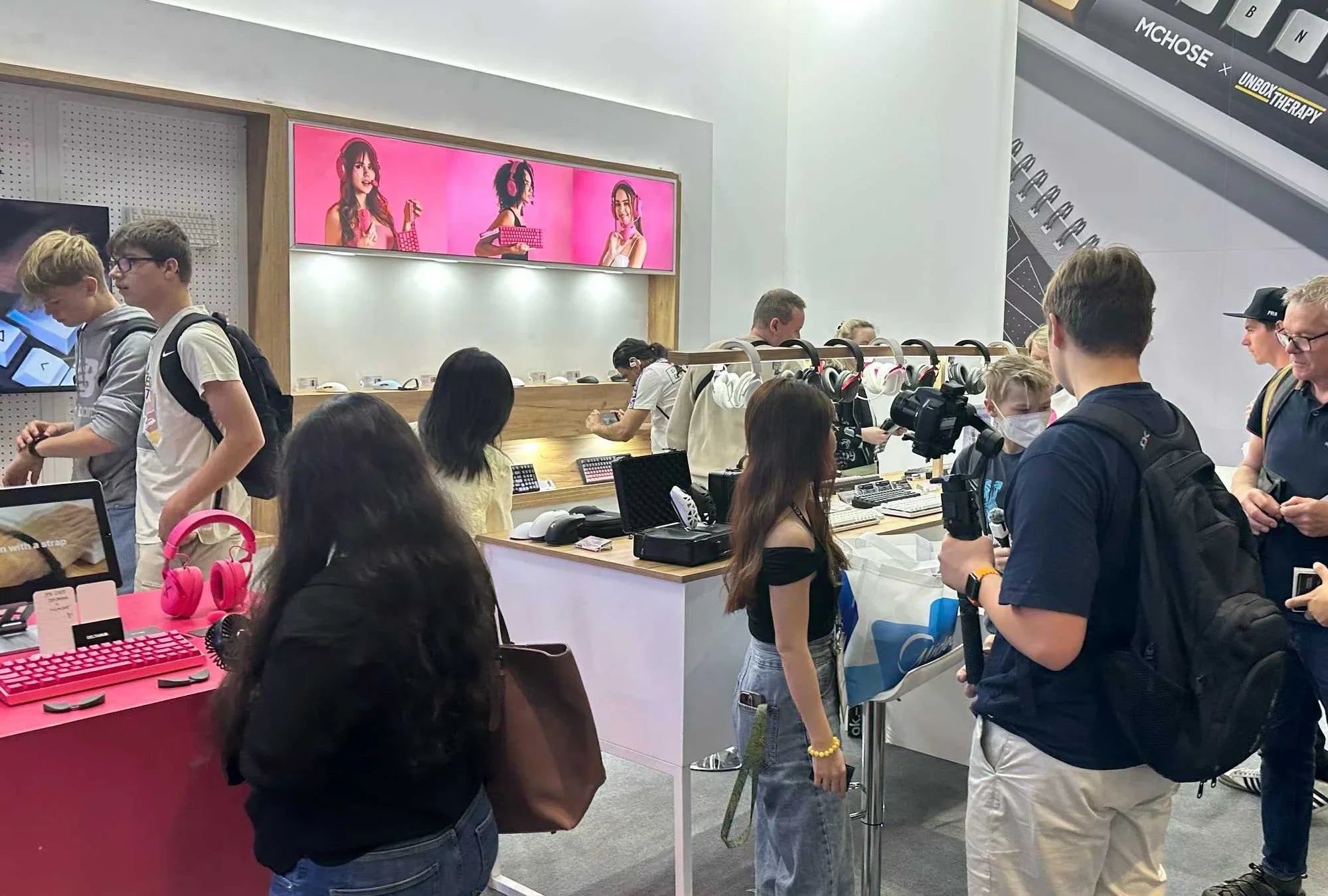 Shoppers browsing pink gaming keyboards and headphones at a tech expo booth