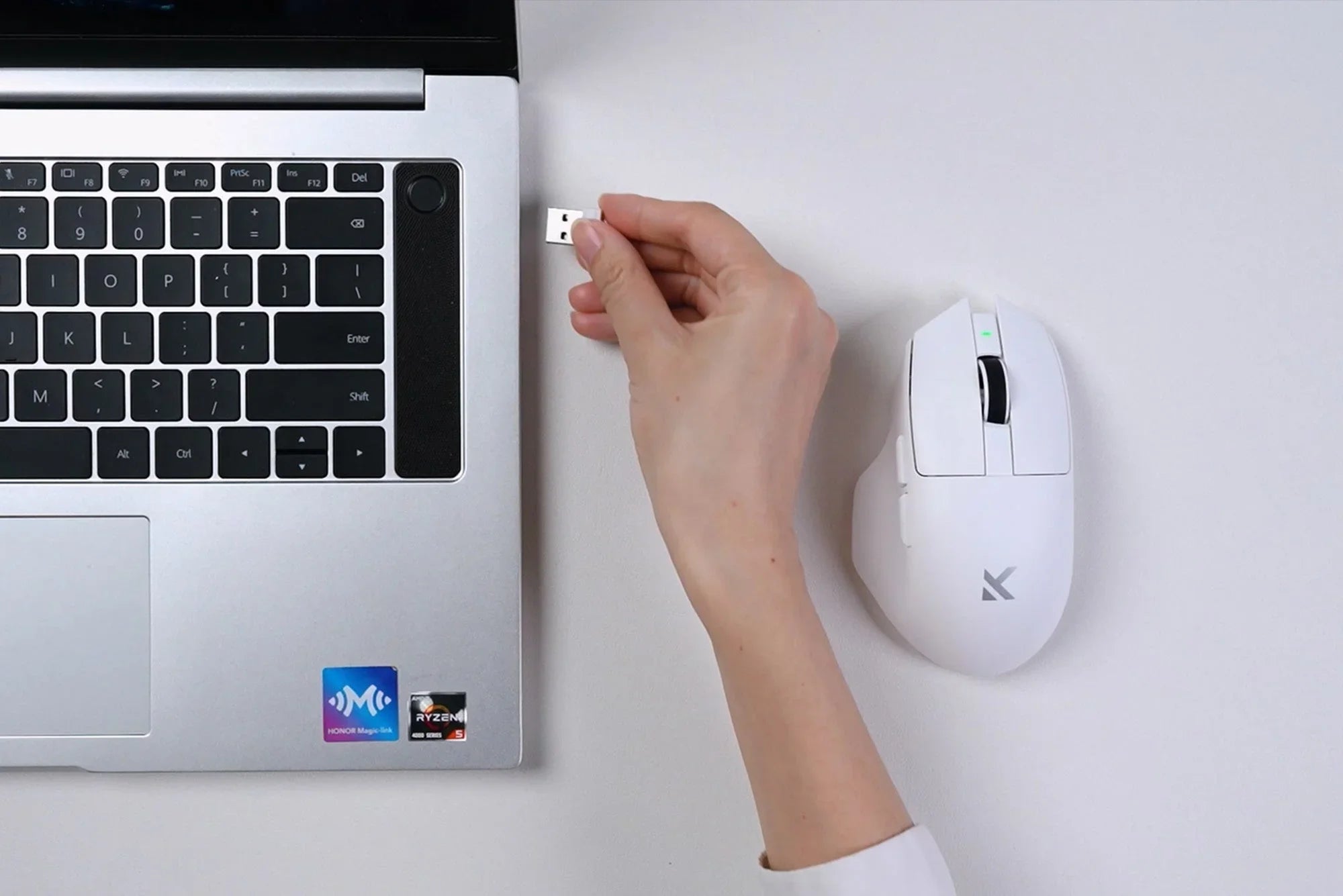 White wireless mouse with USB receiver next to laptop, hand plugging in dongle for seamless connectivity