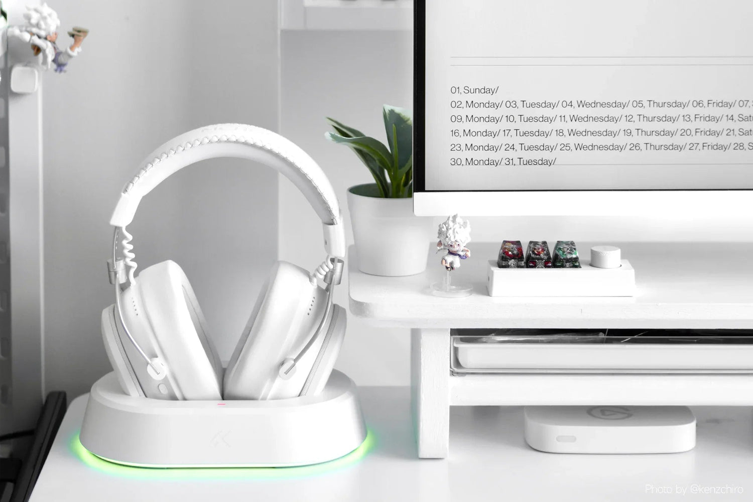 White gaming headphones on charging dock with RGB lighting, minimalist desk setup