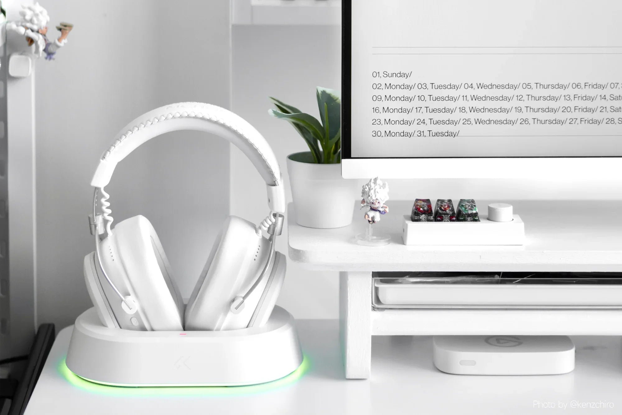 White gaming headphones on charging dock with RGB lighting, minimalist desk setup