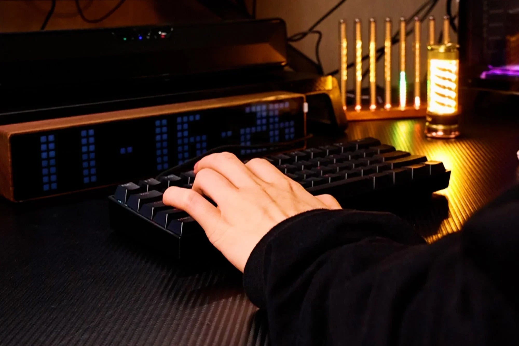Hand typing on black mechanical keyboard with blue LED clock, warm ambient desk lighting